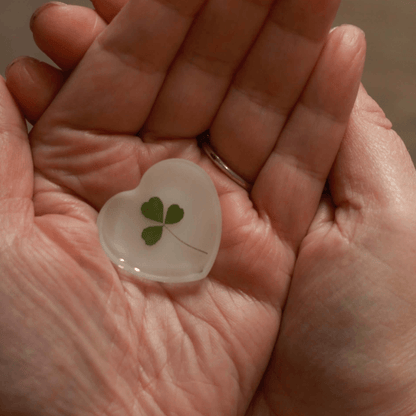 Heart-shaped resin object with a Hand foraged shamrock held between two hands.